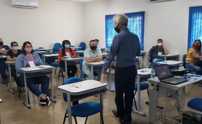 Sala de aula com algumas pessoas sentadas e um senhor de pé que fala a elas